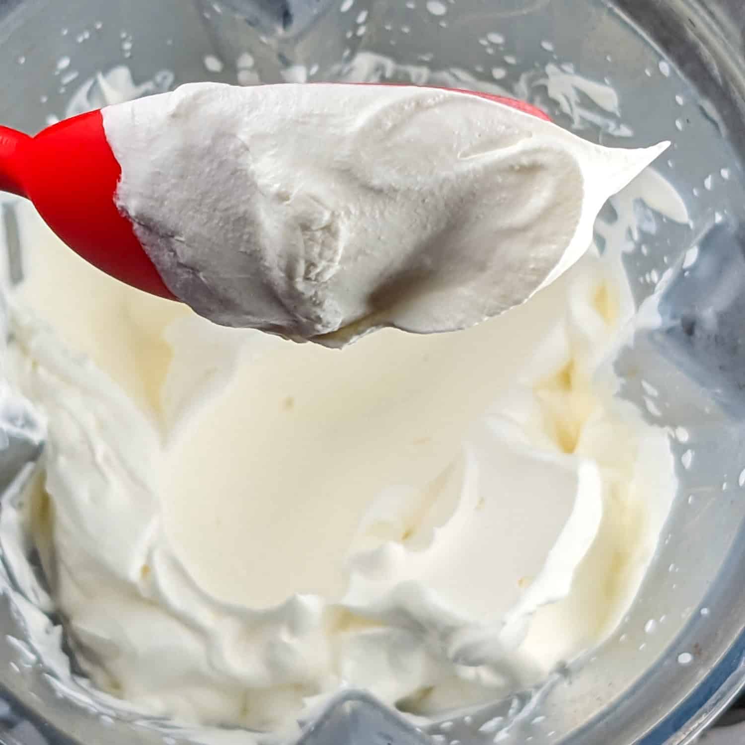 Creamy whipped cream in a blender, showcasing a red silicone spoon for no-churn ice cream.